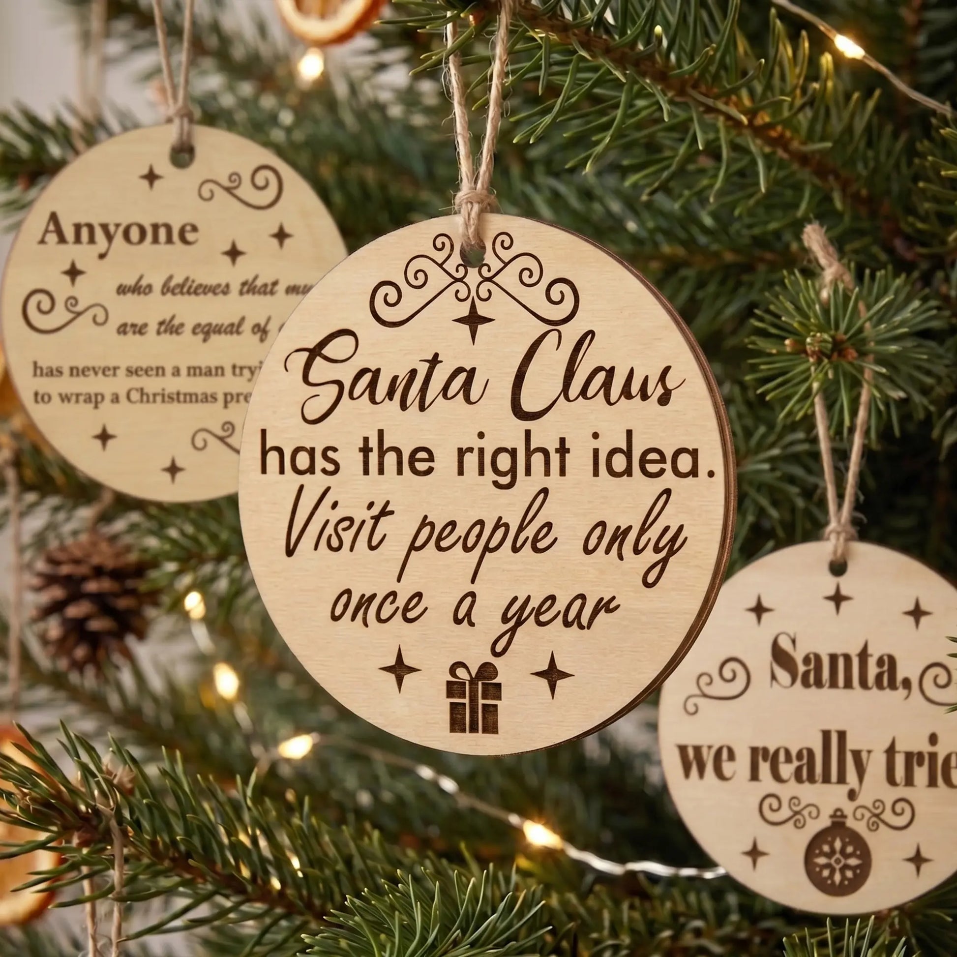 Group of round laser cut plywood Christmas ornaments with funny quotes hanging on a festive pine tree with twinkling lights.