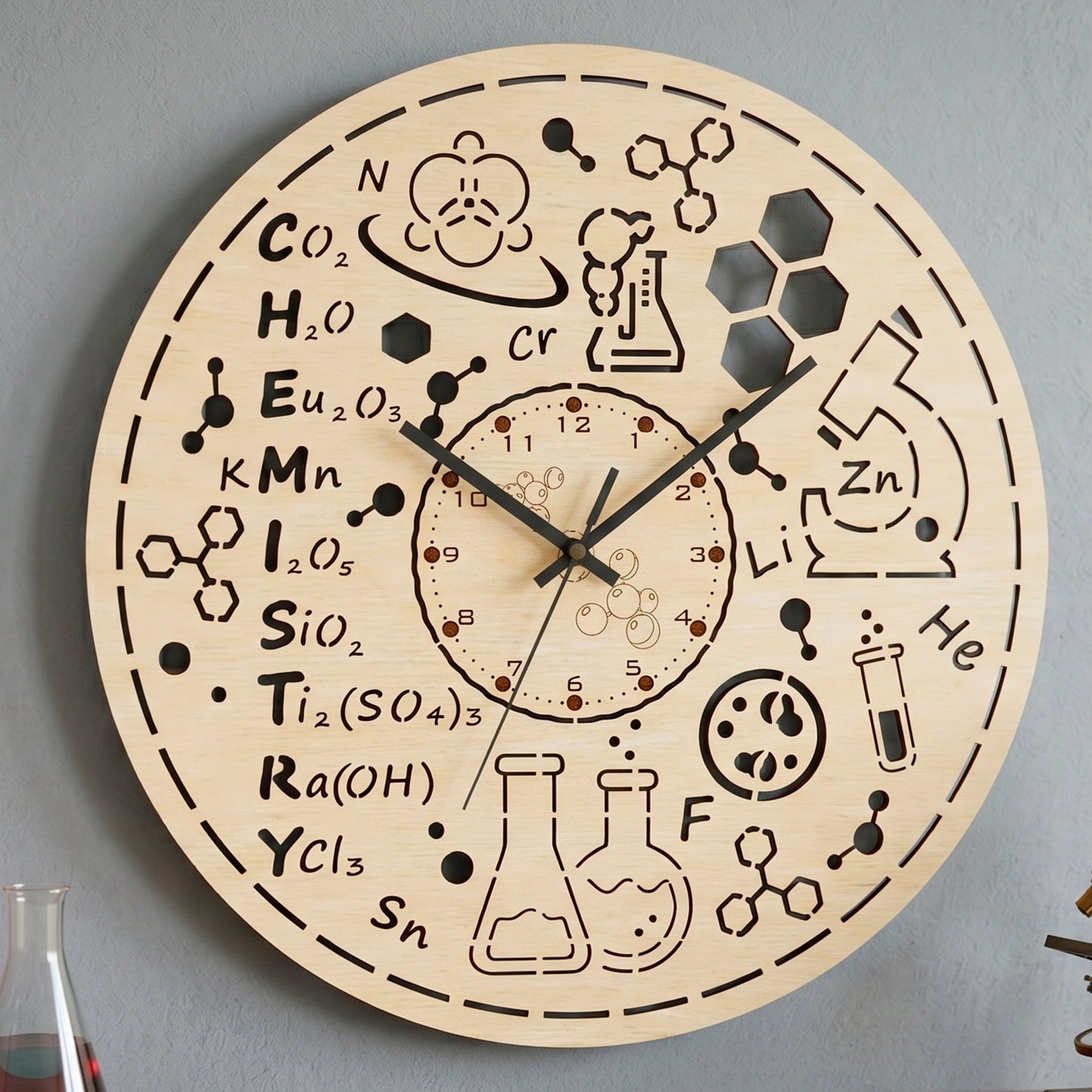 Laser cut plywood chemistry wall clock hanging on a gray wall, featuring engraved science formulas and cut out design