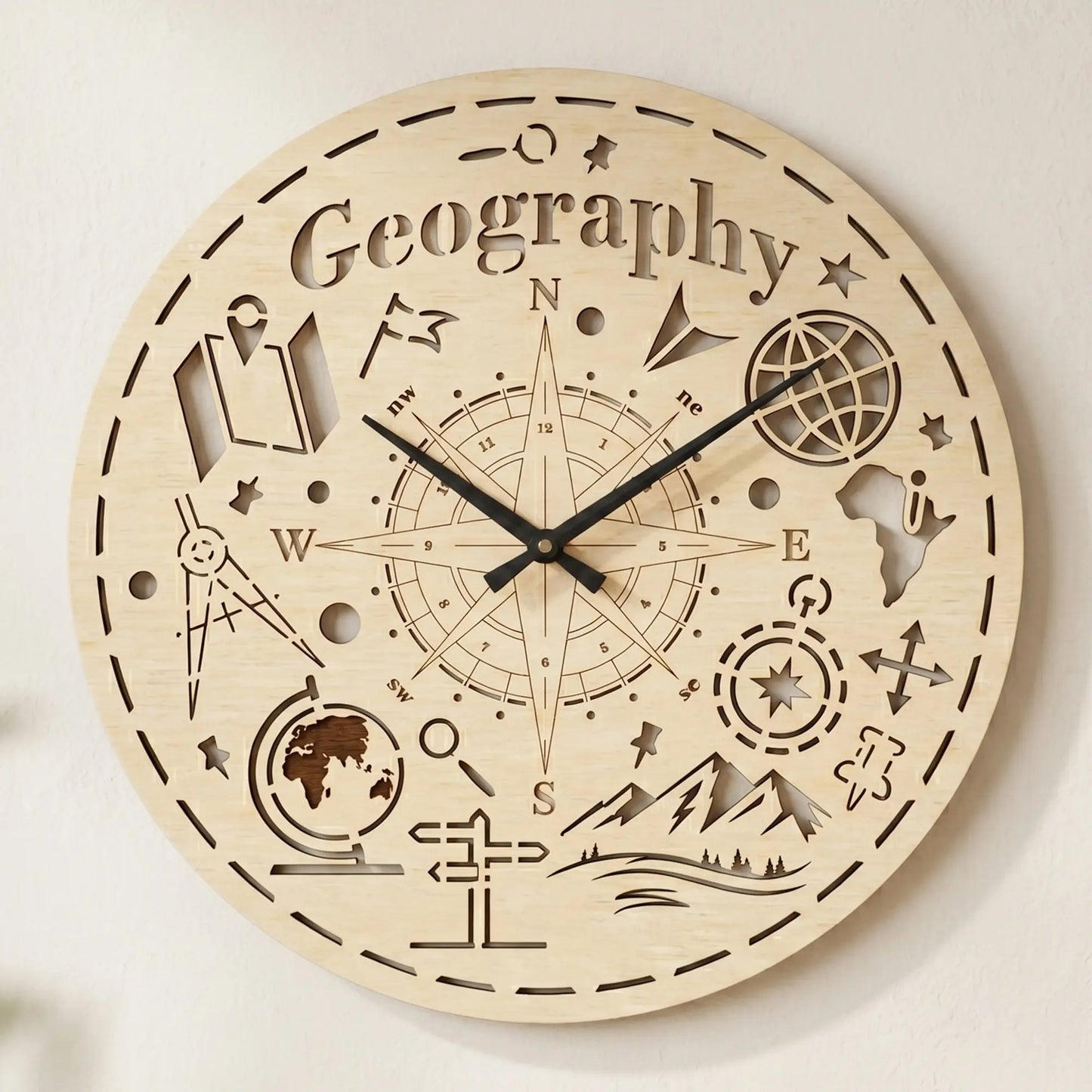 Round laser cut plywood wall clock featuring 'Geography' text, a large compass rose, globe, and mountain icons on white wall