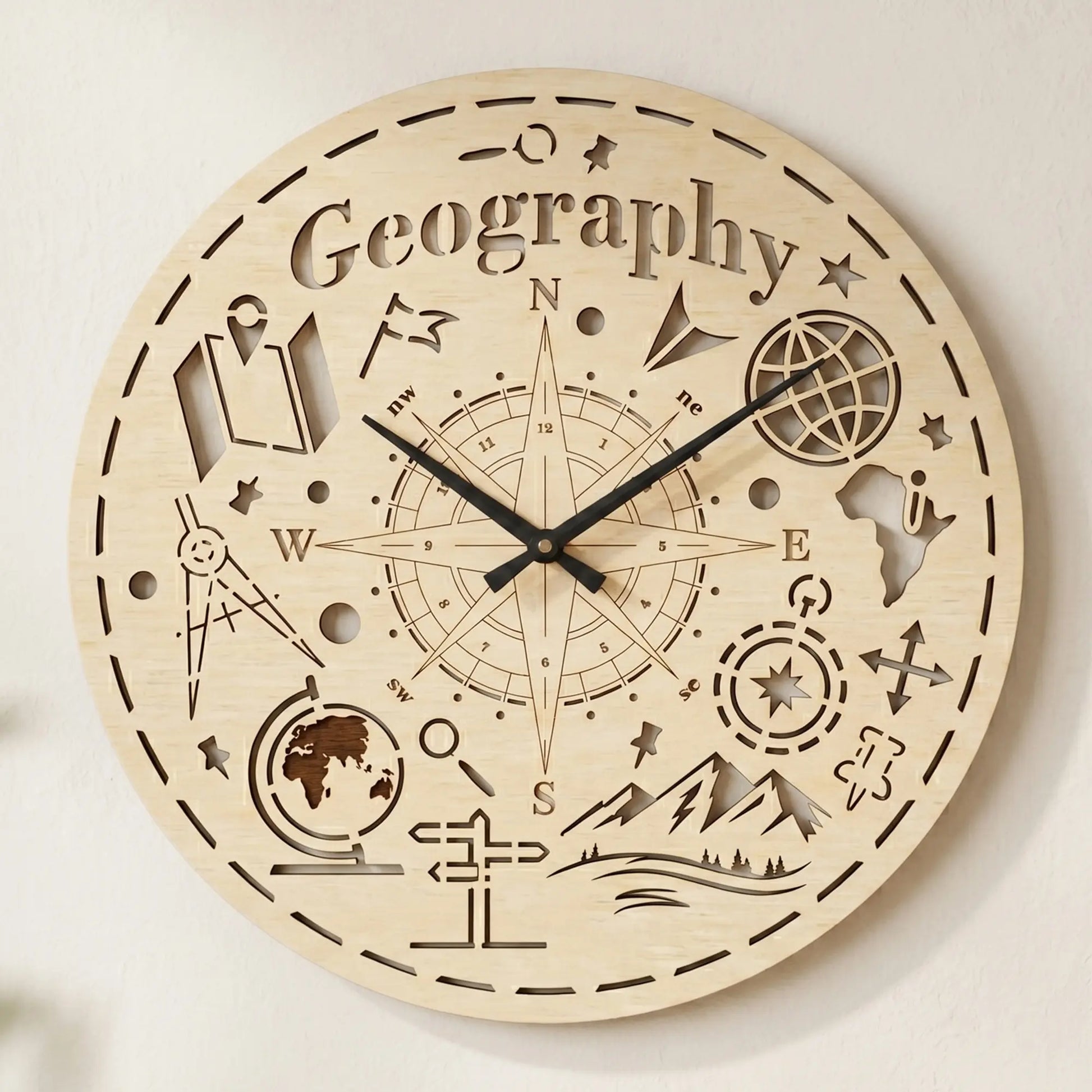 Round laser cut plywood wall clock featuring 'Geography' text, a large compass rose, globe, and mountain icons on white wall