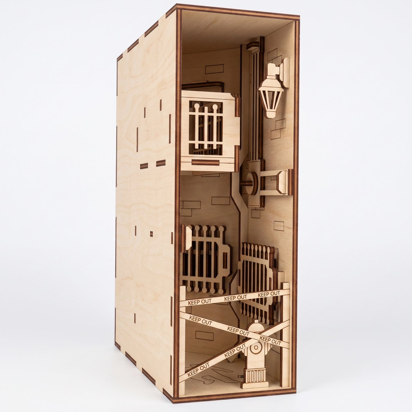 Three-quarter view of a laser-cut birch plywood crime scene book nook with a balcony, barrier tape, and dark burnt edges.