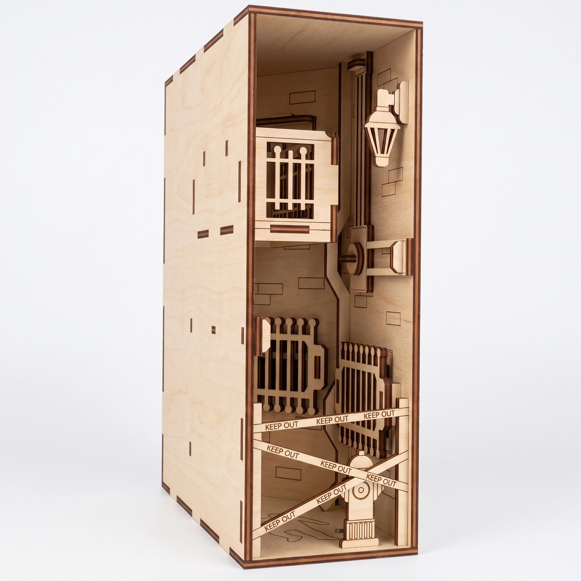 Three-quarter view of a laser-cut birch plywood crime scene book nook with a balcony, barrier tape, and dark burnt edges.