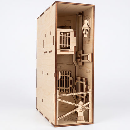 Three-quarter view of a laser-cut birch plywood crime scene book nook with a balcony, barrier tape, and dark burnt edges.