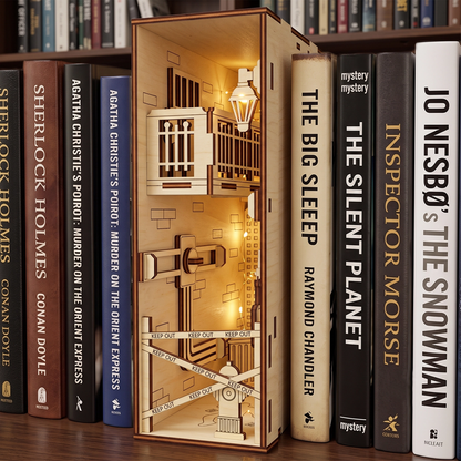 Lit laser-cut birch plywood crime scene book nook on a shelf between mystery books, featuring warm internal lights.