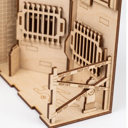 Close-up of a laser-cut birch plywood crime scene book nook with "Keep Out" barrier tape, a hydrant, and dark burnt edges