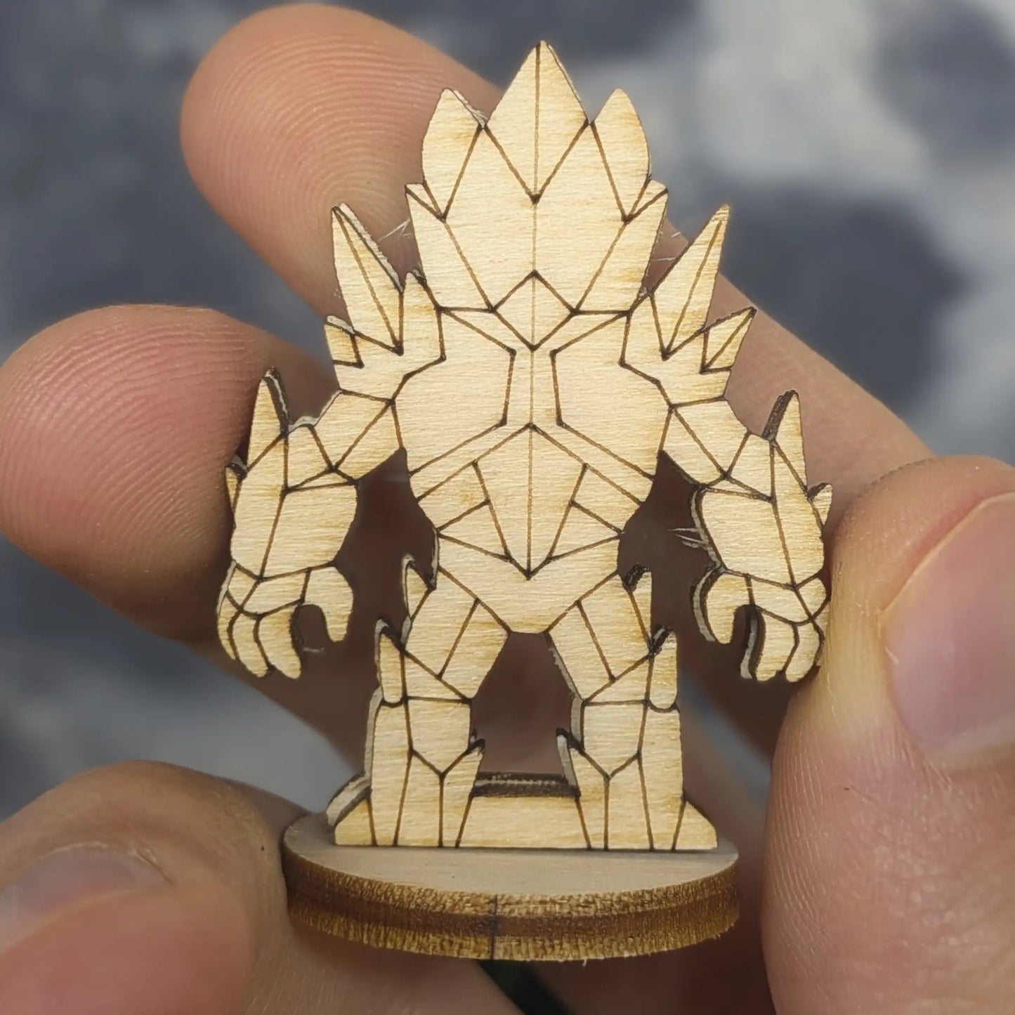 Back view of a crystal golem miniature of laser cut plywood held in hand. Highlights faceted crystal patterns and dark edges