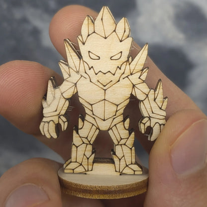 Hand holds a laser cut plywood crystal golem. Detailed engravings show sharp teeth, blank eyes, and jagged crystal facets.