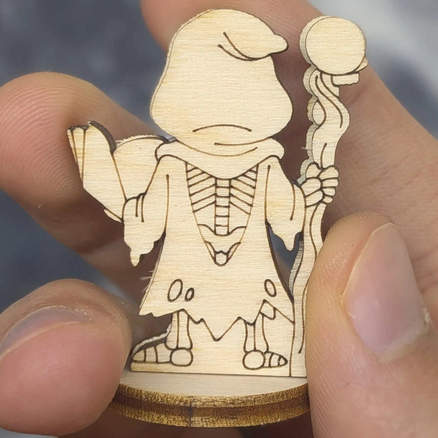 Back view of a laser cut plywood dark necromancer held in hand. Highlights the dark burnt edges and smooth wood textures