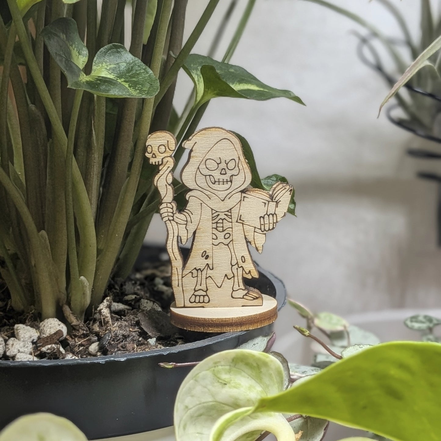 A dark necromancer of laser cut plywood stands in a plant pot. Features a skull staff and tattered robes on natural wood