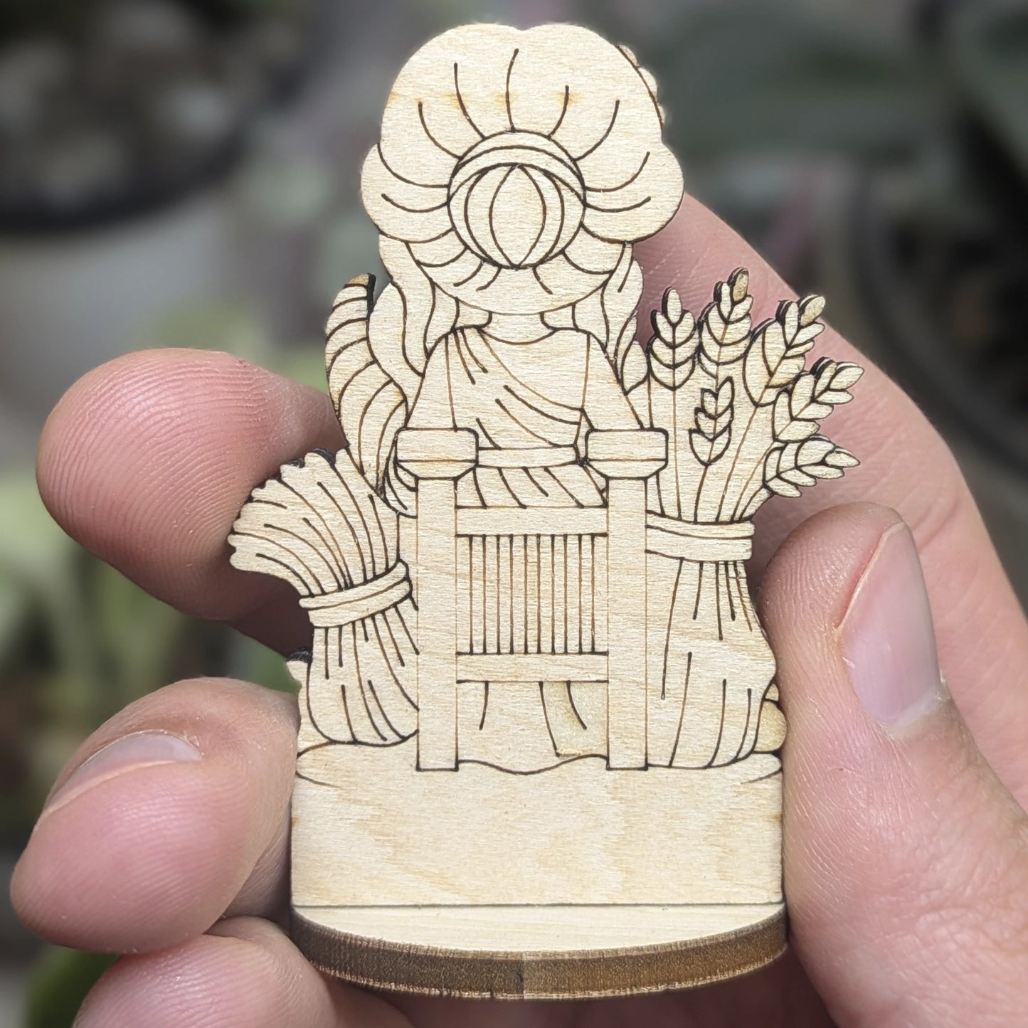 Back view of a laser cut plywood Demeter held in hand. Shows dark burnt wood edges, flowing hair, and natural grain texture