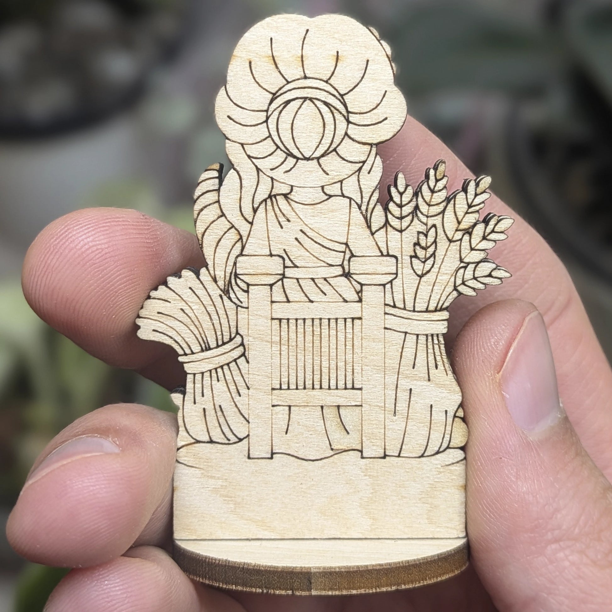 Back view of a laser cut plywood Demeter held in hand. Shows dark burnt wood edges, flowing hair, and natural grain texture
