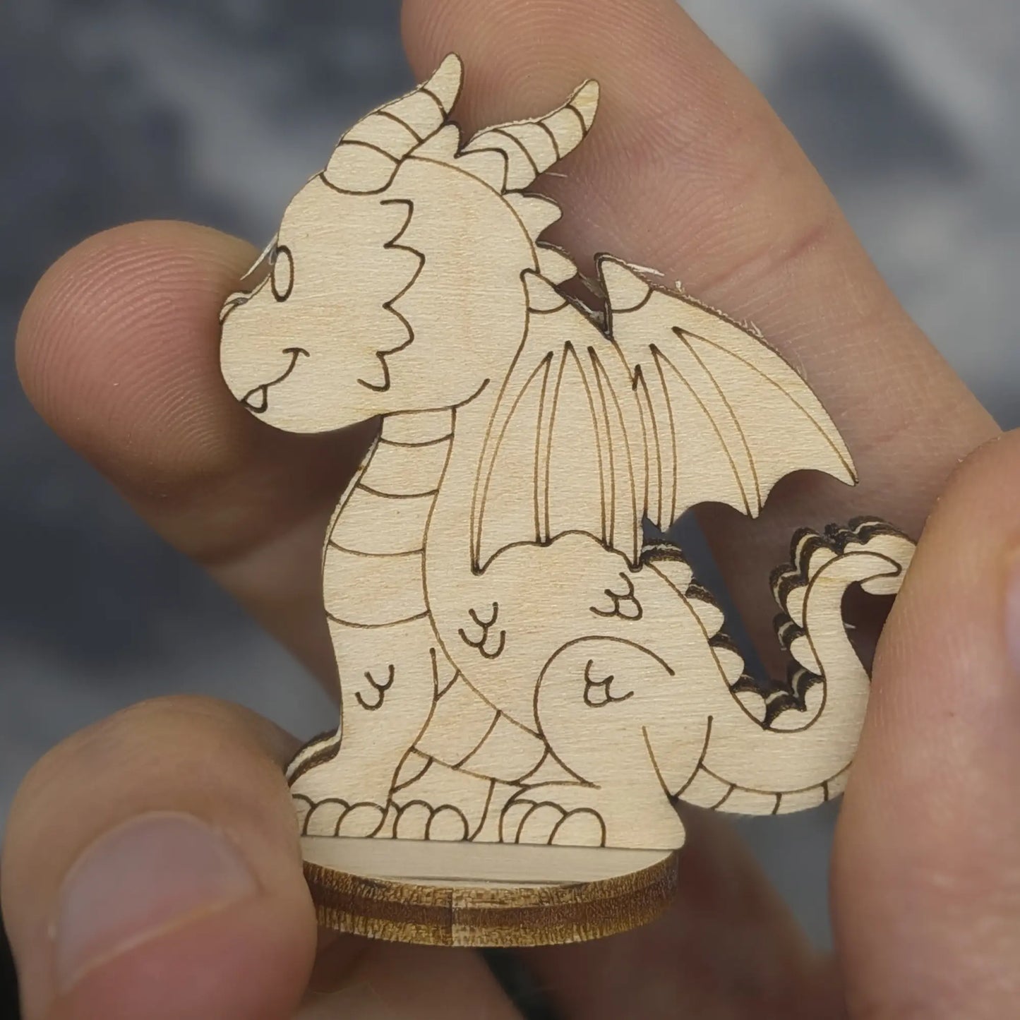Back view of a laser cut plywood dragon held in hand. Shows dark burnt edges, wing details, and a spiked tail on wood base