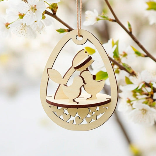 Laser-cut plywood wooden Easter egg ornament hanging from a white flowering cherry branch. The egg-shaped frame features a layered scene inside with two baby chicks, a tulip, and a base decorated with cutout hearts