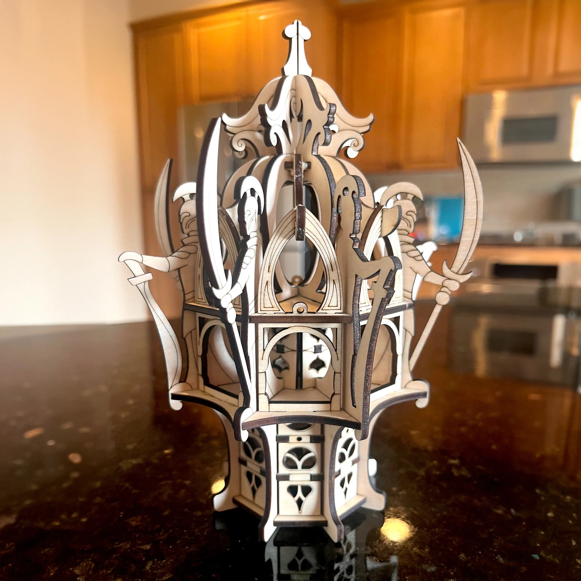 Assembled laser cut plywood elven tower centerpiece standing on a glossy dark kitchen countertop with warm lighting.