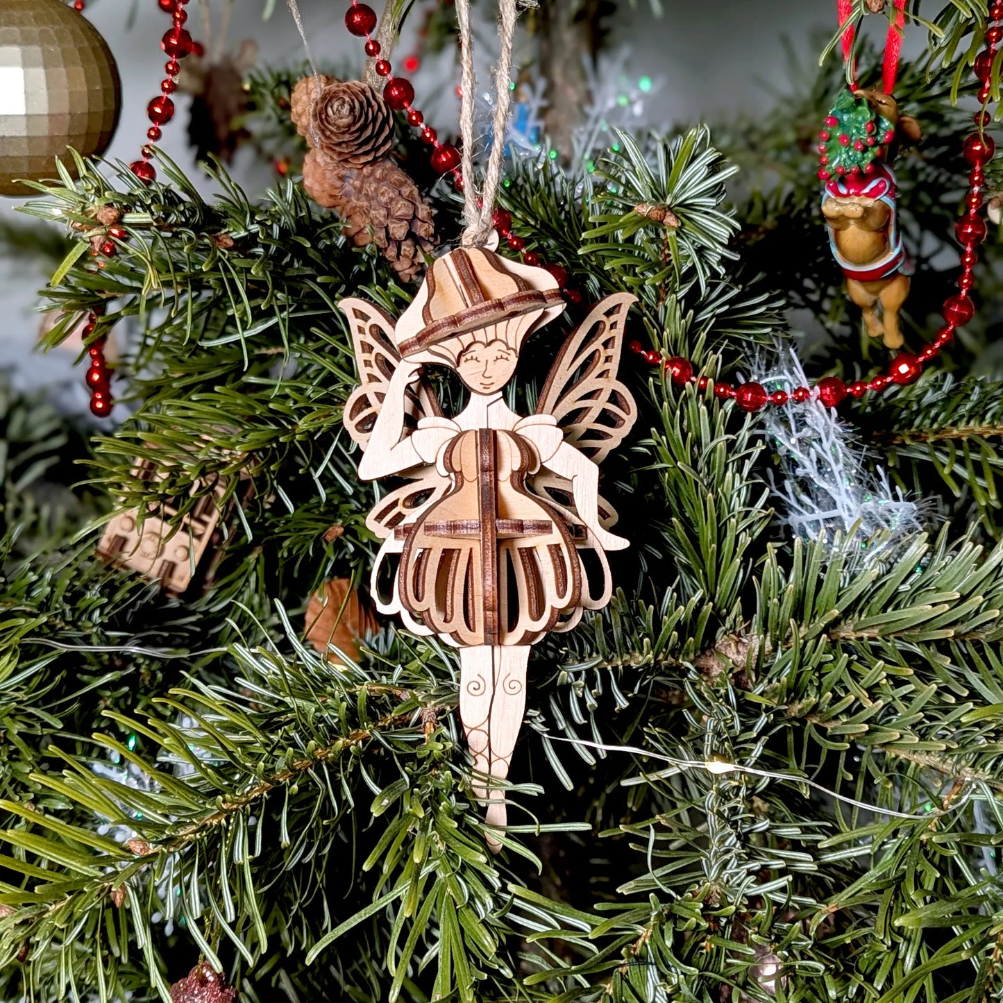 Laser cut plywood mushroom fairy ornament hanging on a Christmas tree branch.