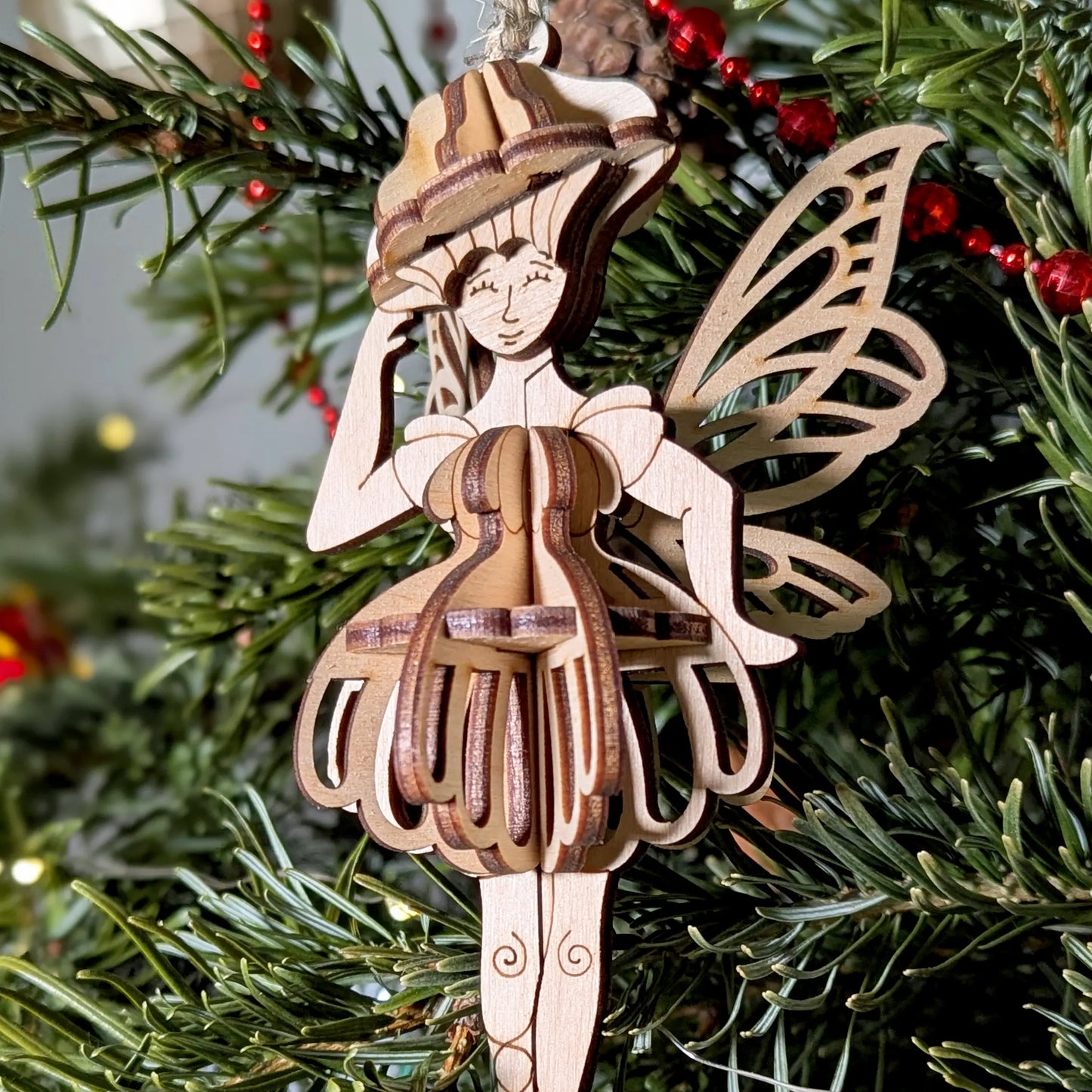 Close-up of a laser cut plywood fairy with intricate wing details and 3D layered dress on a tree.