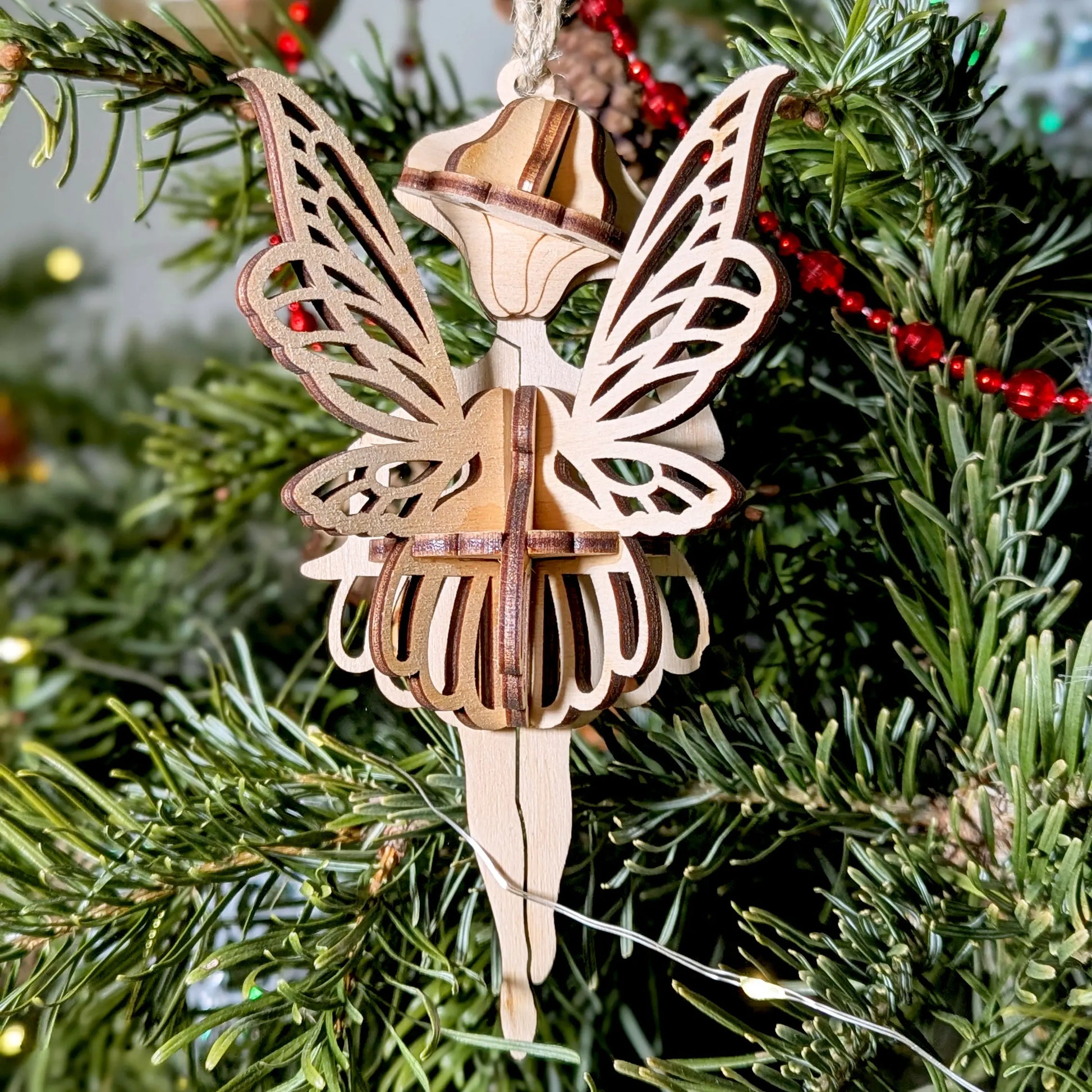Laser cut plywood fairy showing layered 3D skirt and wings on a Christmas tree.