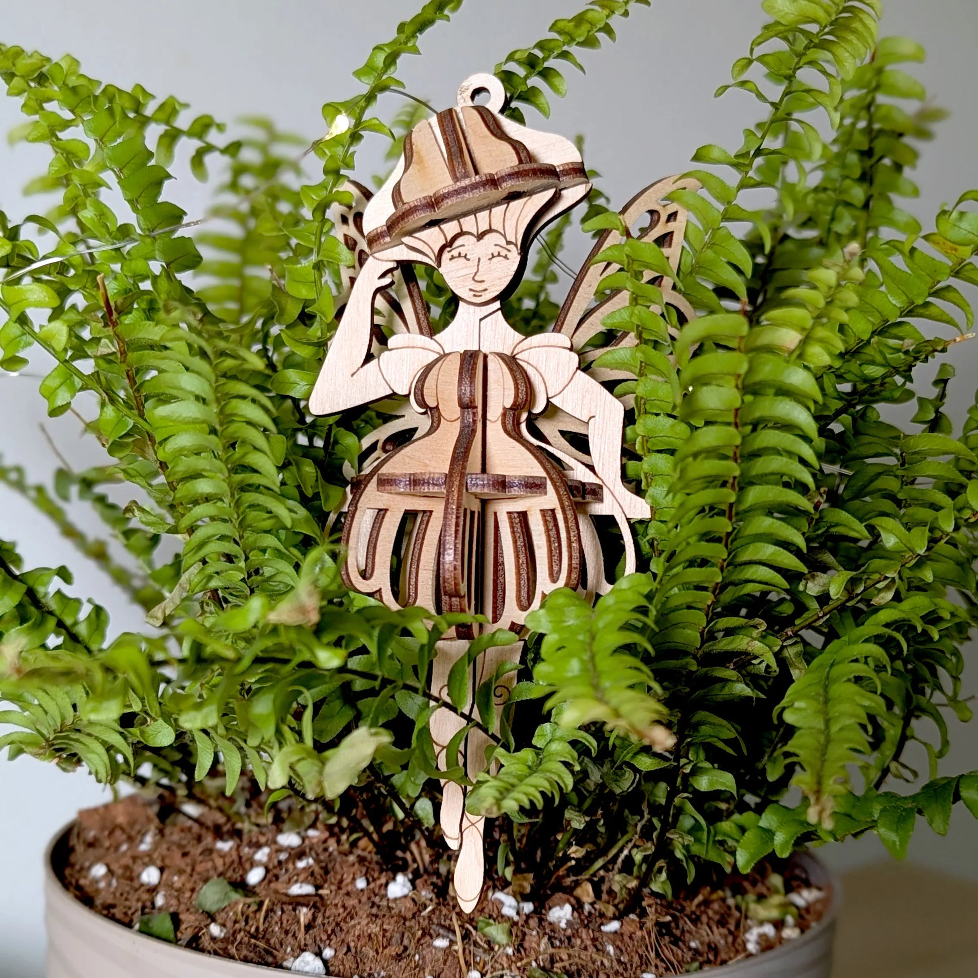 Laser cut plywood mushroom fairy ornament positioned inside a lush green fern plant.