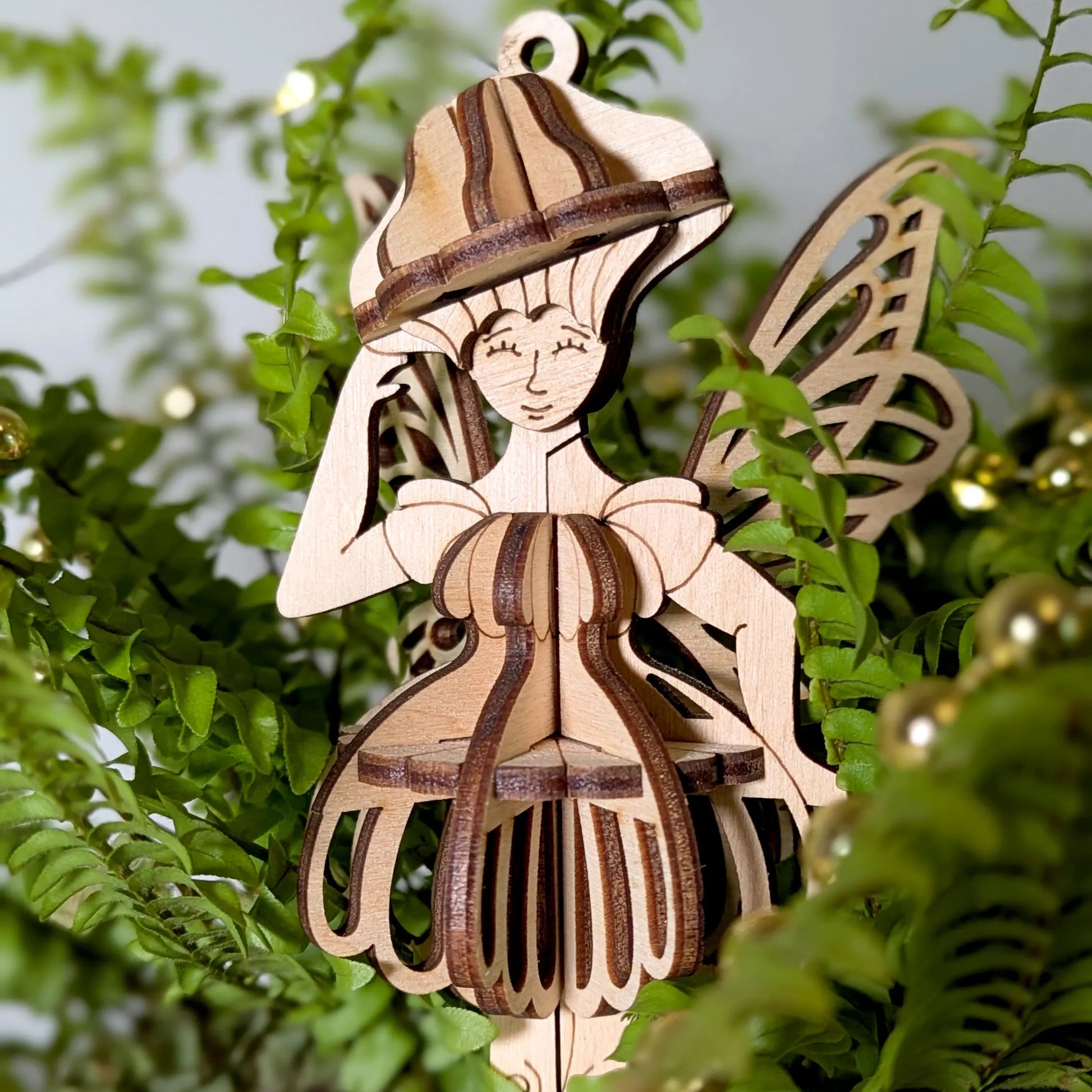 Laser cut plywood mushroom fairy figurine hanging inside a decorative green fern.
