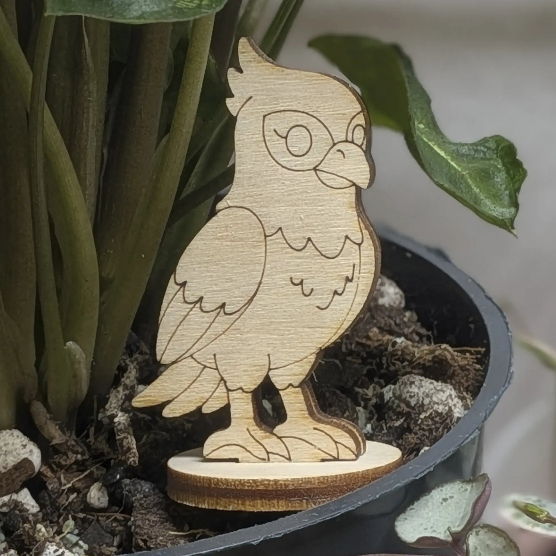 A laser cut plywood falcon figurine sits in a plant pot, featuring engraved wings, crest, and sharp talons on a wood base.