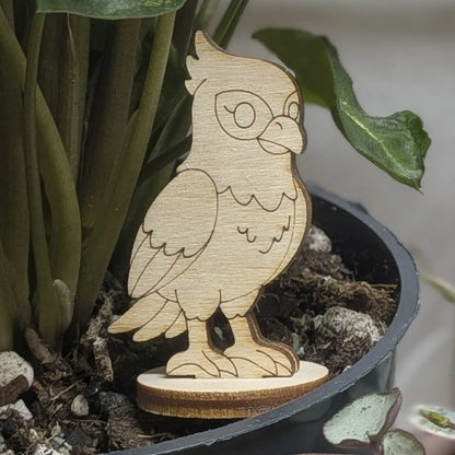 A laser cut plywood falcon figurine sits in a plant pot, featuring engraved wings, crest, and sharp talons on a wood base.