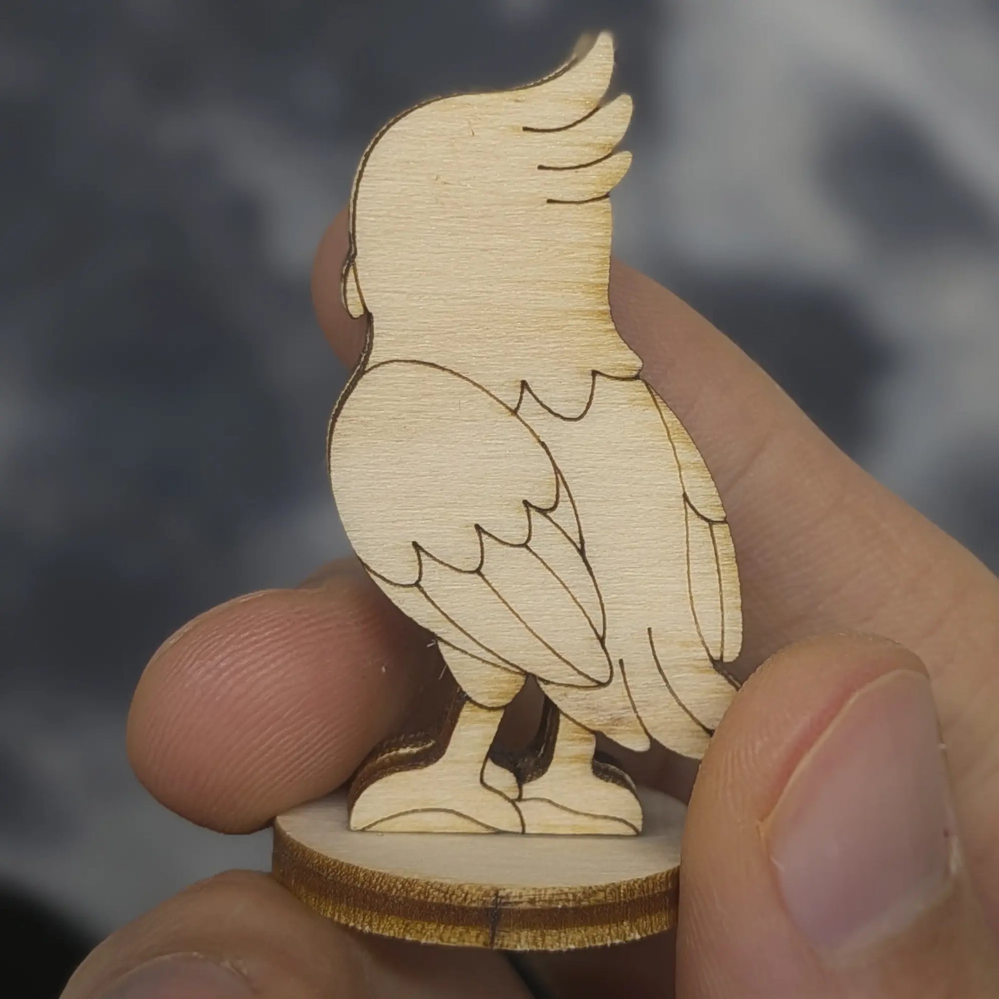A back view of a laser cut plywood falcon held in hand. Highlights the dark burnt edges and intricate wing feather carvings