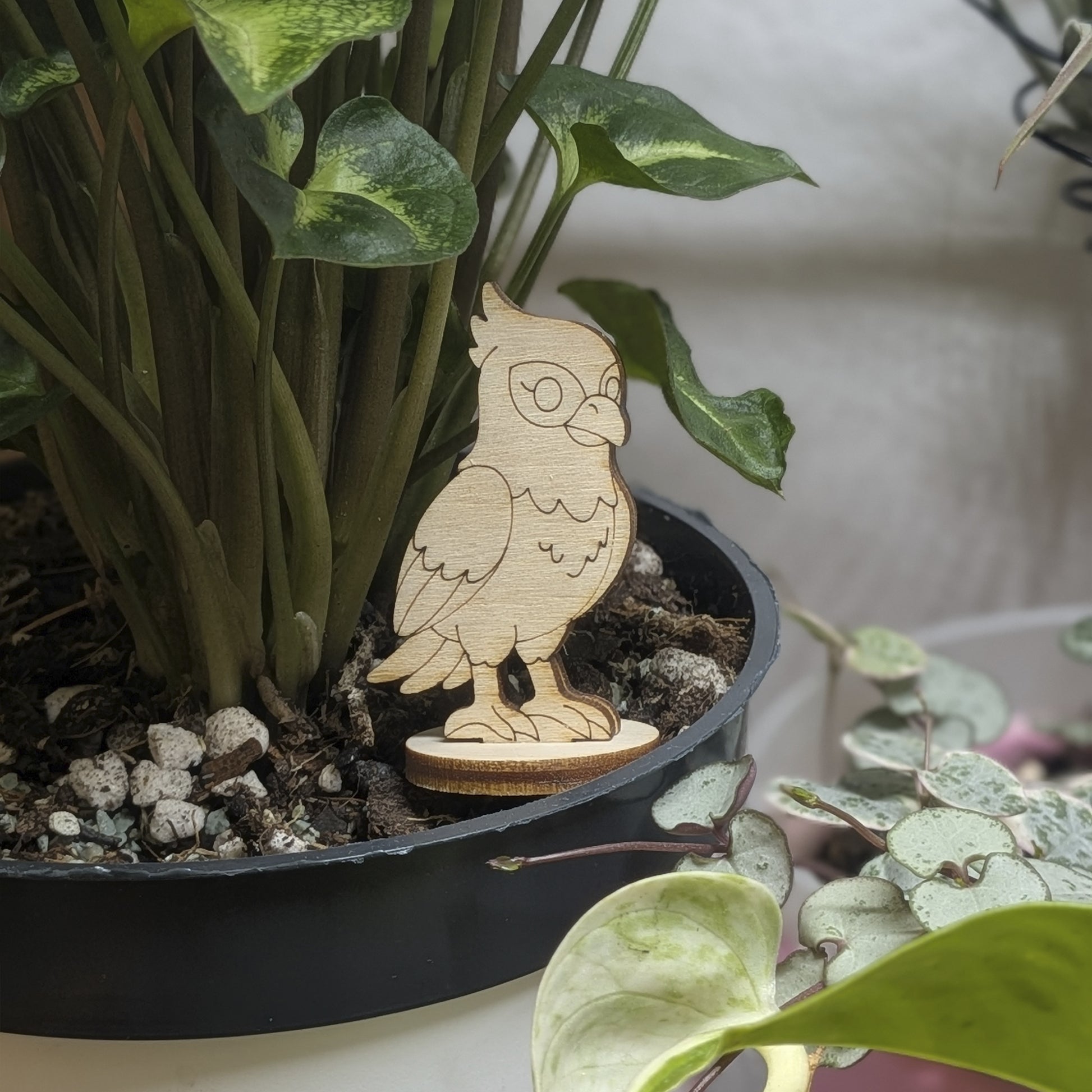 A laser cut plywood falcon figurine sits in a plant pot, featuring engraved wings, crest, and sharp talons on a wood base.