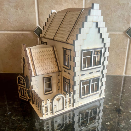 Assembled laser cut plywood family dollhouse with a small fenced yard and heart gate, displayed on a glossy dark surface.