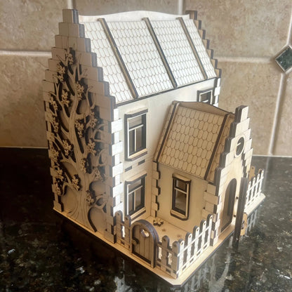 Assembled laser cut plywood family house showing the beautifully engraved blooming tree on the side wall and a front yard.