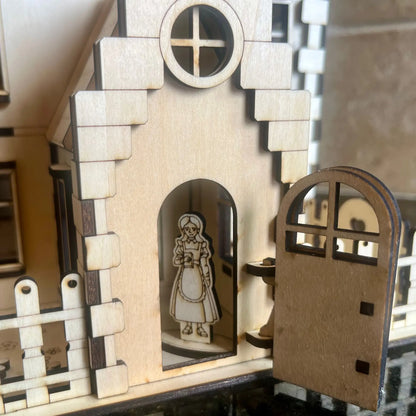 Close-up of the open front wooden door showing a miniature girl figurine inside a laser cut plywood family dollhouse kit.