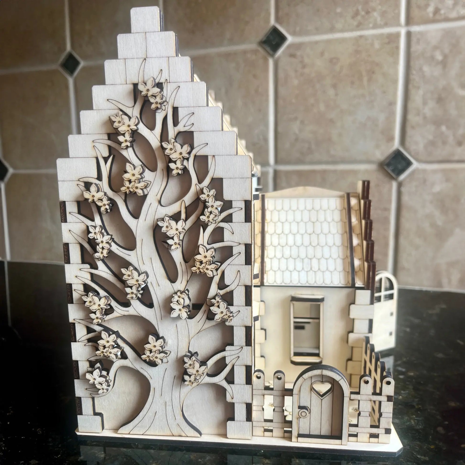 Detailed side shot focusing on a large engraved blooming tree on the stepped gable wall of a laser cut plywood house.