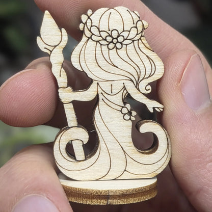 Back view of a laser cut plywood dryad held in hand. Shows dark burnt edges, natural wood grain, and leafy hair texture