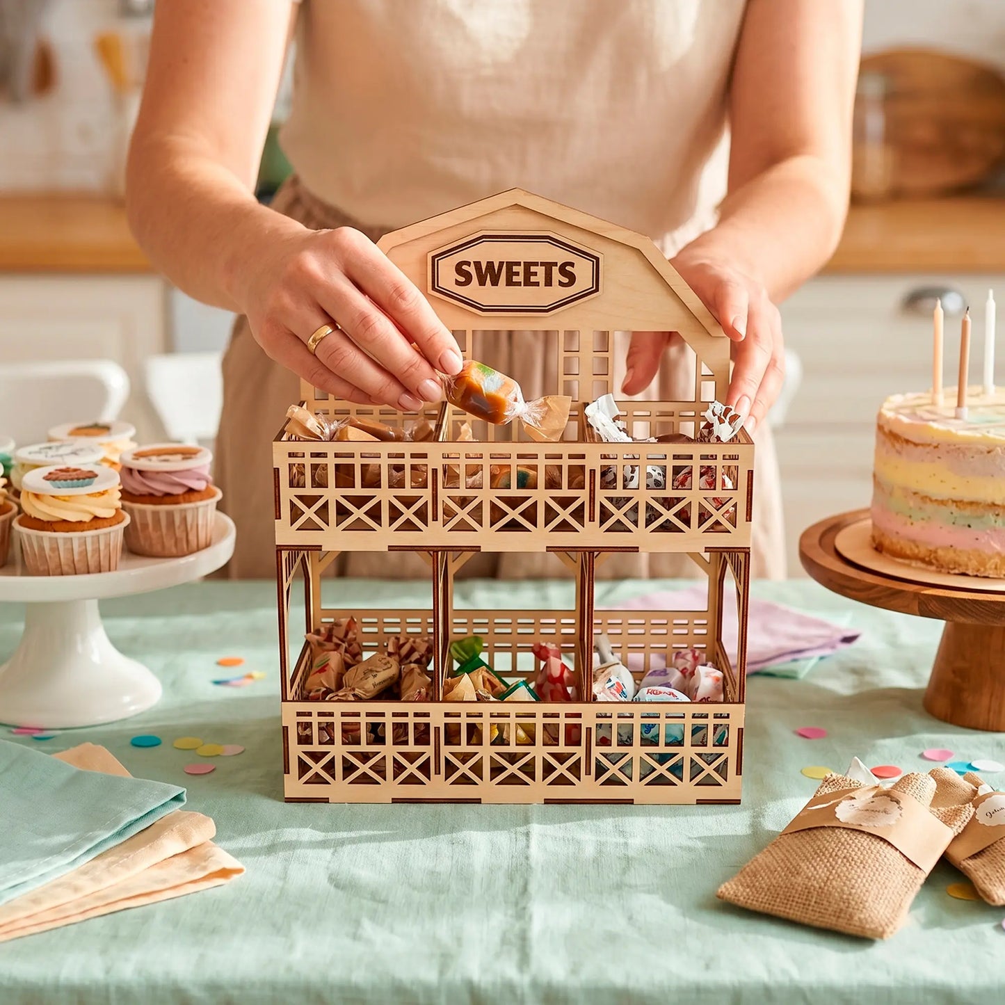 Laser cut plywood barn tier stand filled with candies on a birthday party table with cupcakes and woman hands