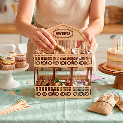 Laser cut plywood barn tier stand filled with candies on a birthday party table with cupcakes and woman hands