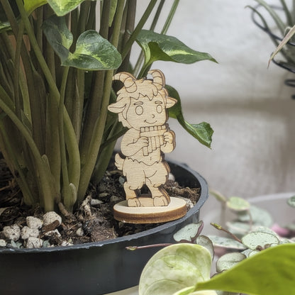 Laser cut plywood faun figurine staged in a plant pot. He plays panpipes amidst green leaves on a sturdy round wood base