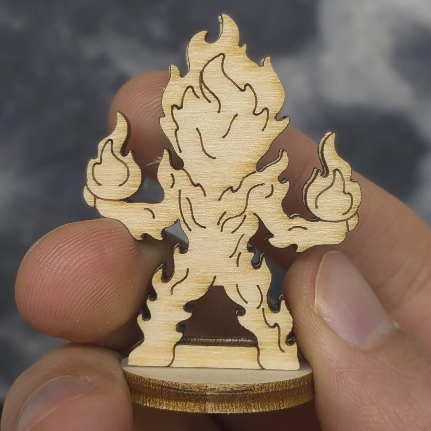 Back view of a laser cut plywood fire elemental held in hand. Highlights the dark burnt edges and natural wood grain finish