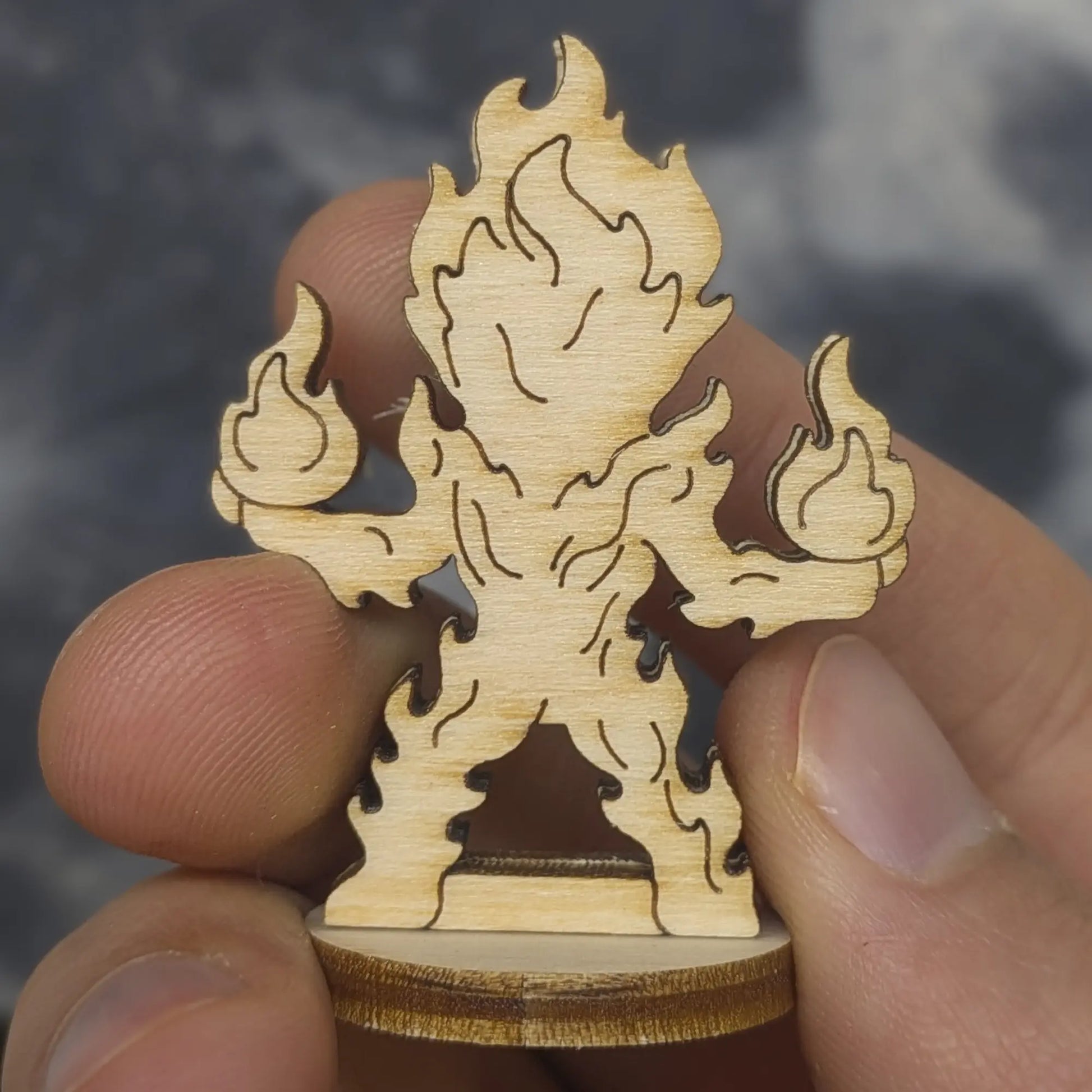 Back view of a laser cut plywood fire elemental held in hand. Highlights the dark burnt edges and natural wood grain finish