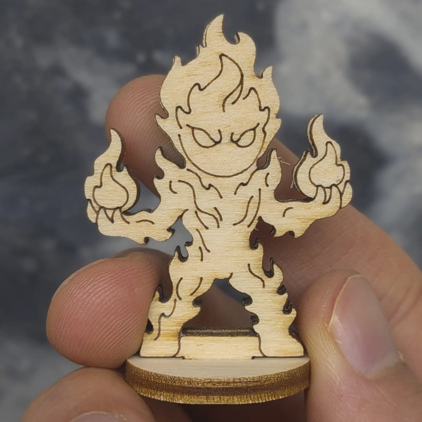 Hand holds a laser cut plywood fire elemental figurine. Detailed front view showing etched flame patterns and wood texture
