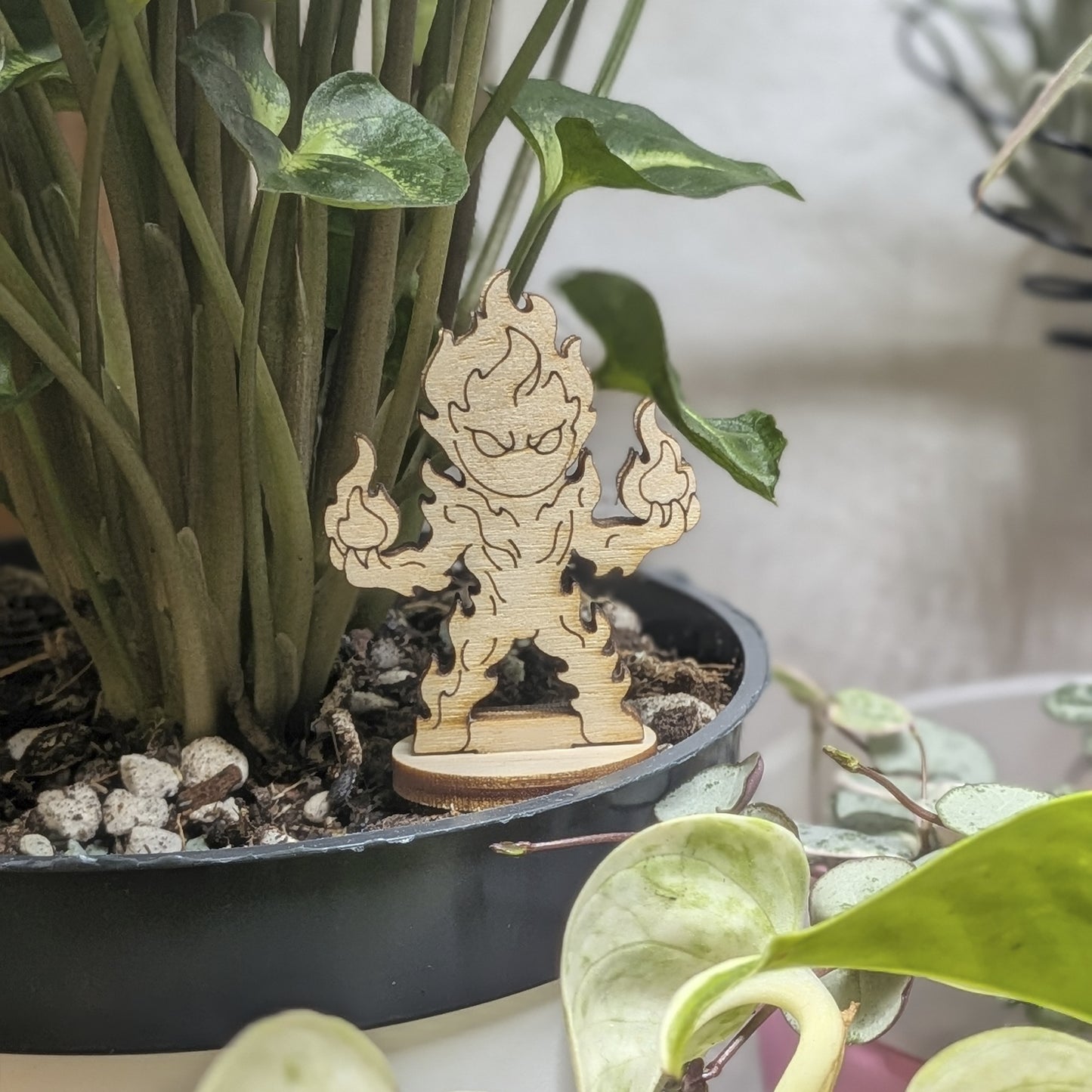 Fire elemental of laser cut plywood sits in a plant pot. Features engraved flame swirls and a tiered fire-shaped body on base