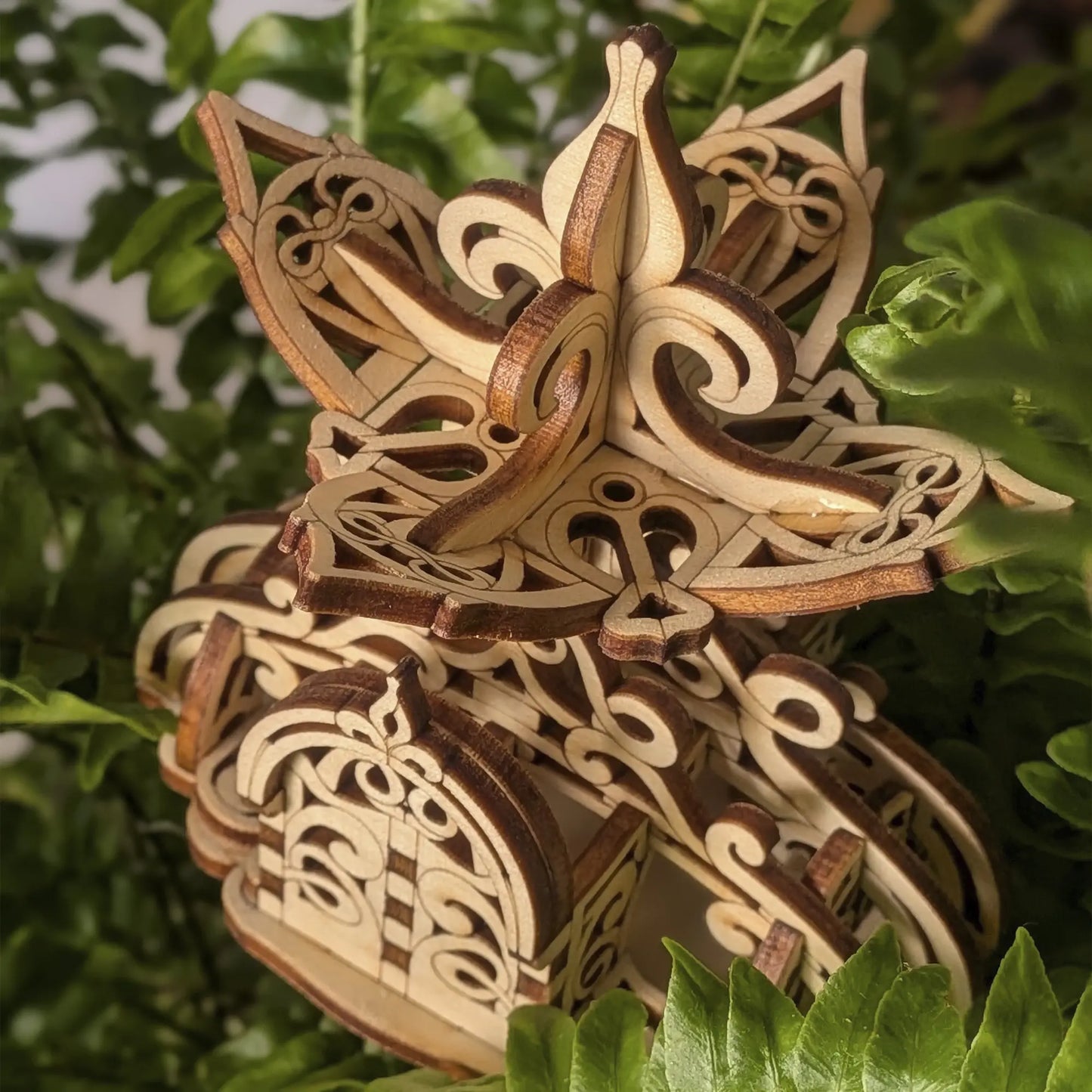 Macro of laser cut plywood fairy house showing dark burnt edges on scrollwork and a detailed layered arched front door model.