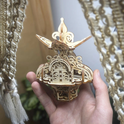 Hand holds the laser cut plywood floral fairy house near plants, showing the model's scale and intricate 3D wood structure.