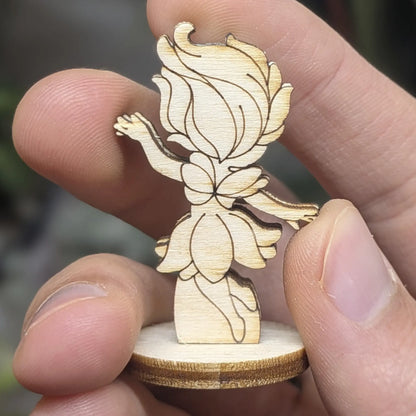 Back view of a laser cut plywood fairy held in fingers, showing wavy hair texture and delicate wings in natural wood grain