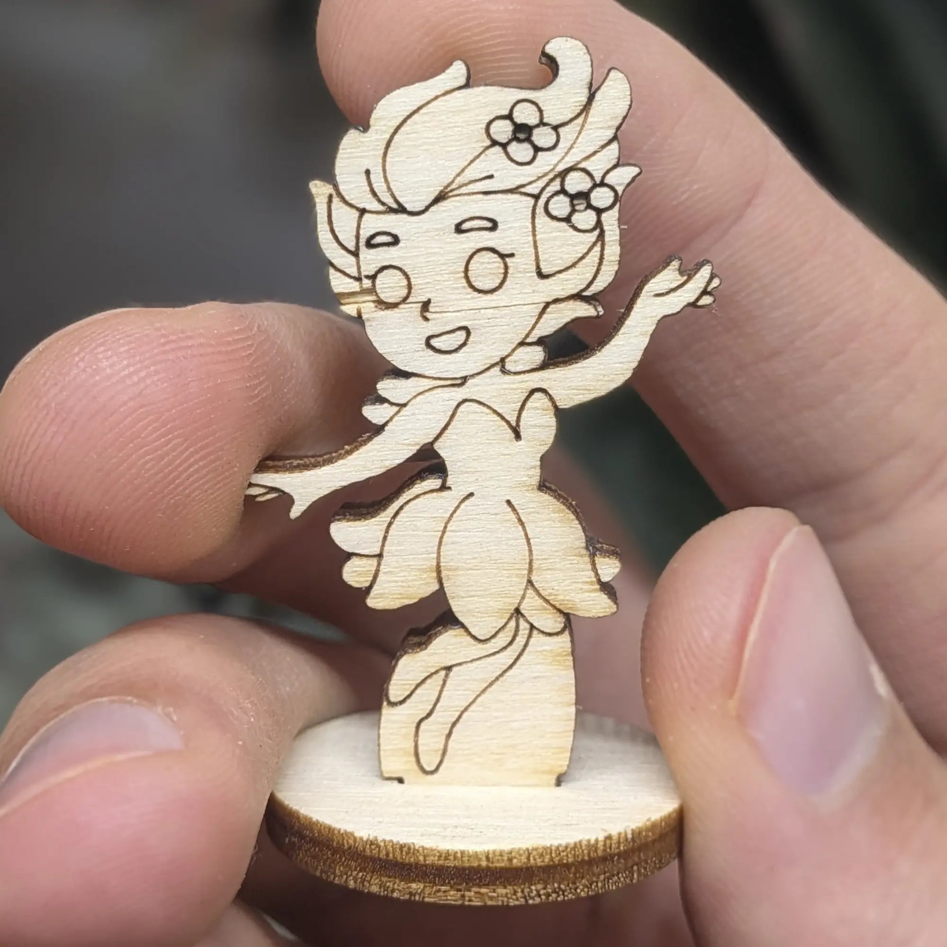 Hand holds a laser cut plywood flower fairy girl for scale. Detailed front view with a petal skirt and cheerful expression