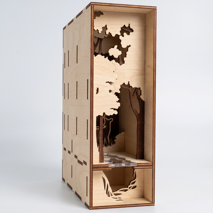 Side view of a laser-cut birch plywood forest book nook showing layered tree cutouts, a deer figure, and natural wood grain