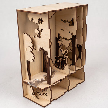 Studio view of a laser-cut birch plywood forest book nook featuring multi-layered trees, a stream, and a deer family figurine