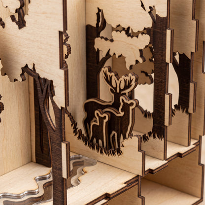 Close-up of a laser-cut birch plywood forest book nook showing layered trees, a deer family, and a stream, with dark burnt edges