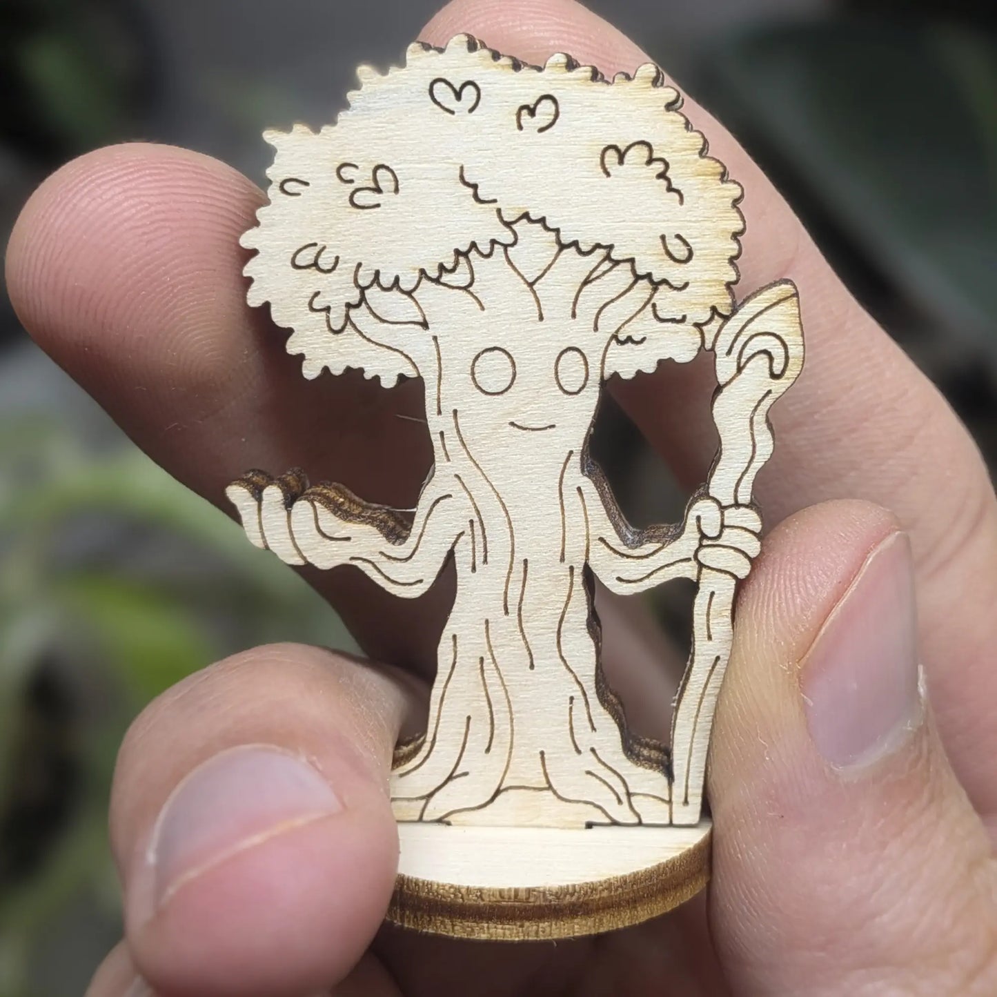 Hand holds a laser cut plywood forest guardian tree. Detailed front view showing the grumpy engraved face and bark texture