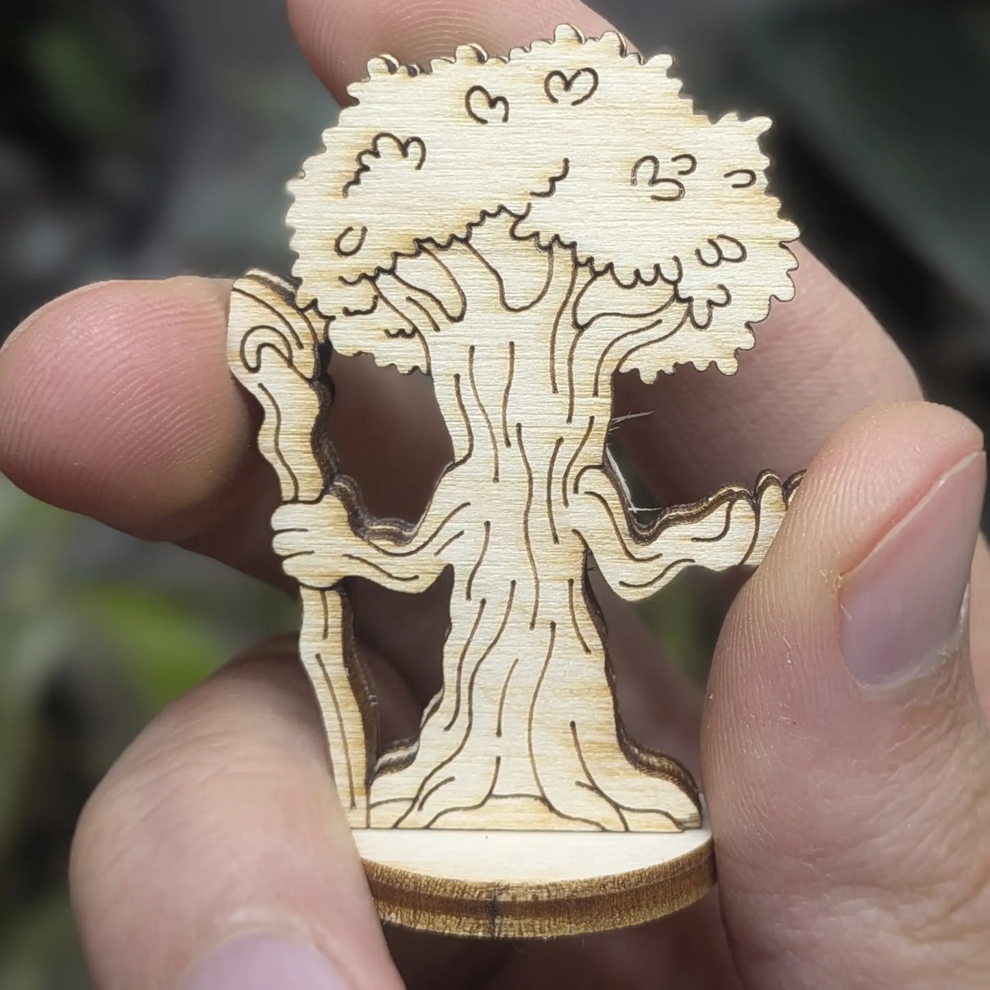 Back view of a laser cut plywood forest guardian tree held in hand. Highlights leafy engravings and dark burnt wood edges