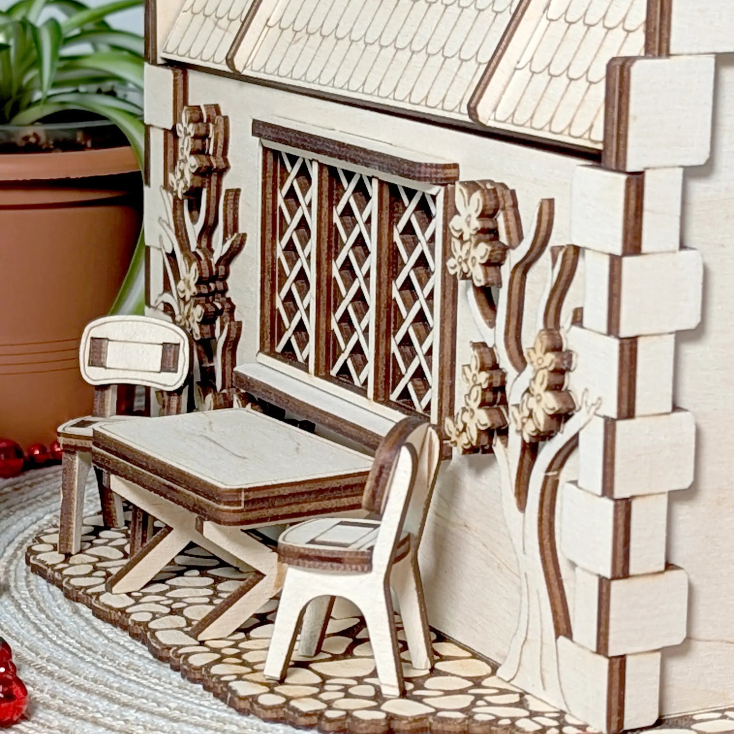 A detailed close-up view of a tiny wooden patio table and two chairs outside a completed laser cut plywood garden cottage.