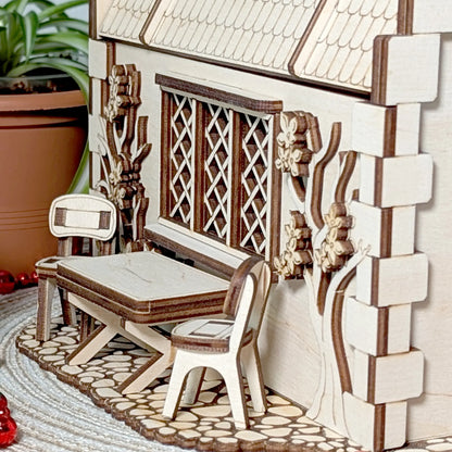 A detailed close-up view of a tiny wooden patio table and two chairs outside a completed laser cut plywood garden cottage.
